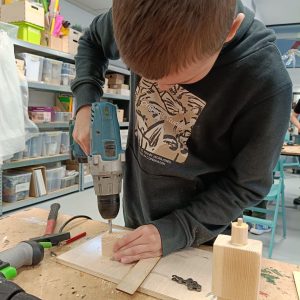 chłopiec robiący dziurę w drewnie wiertarką