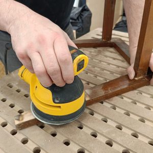 Dłoń trzymająca szlifierkę i szlifująca stary mebel